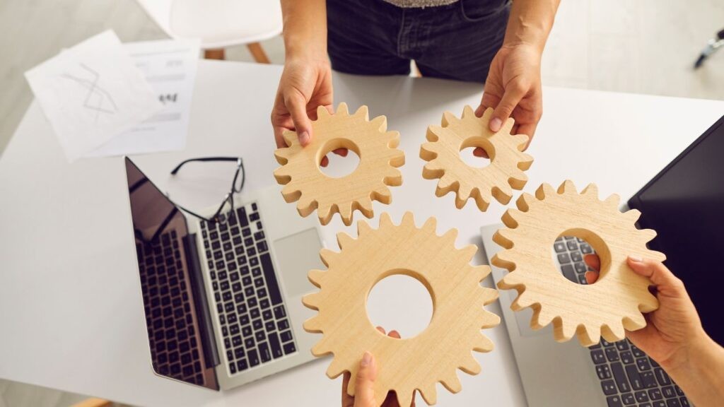 Team members holding wooden gears above laptops, symbolising collaboration, strategy, and choosing the right IT services provider.