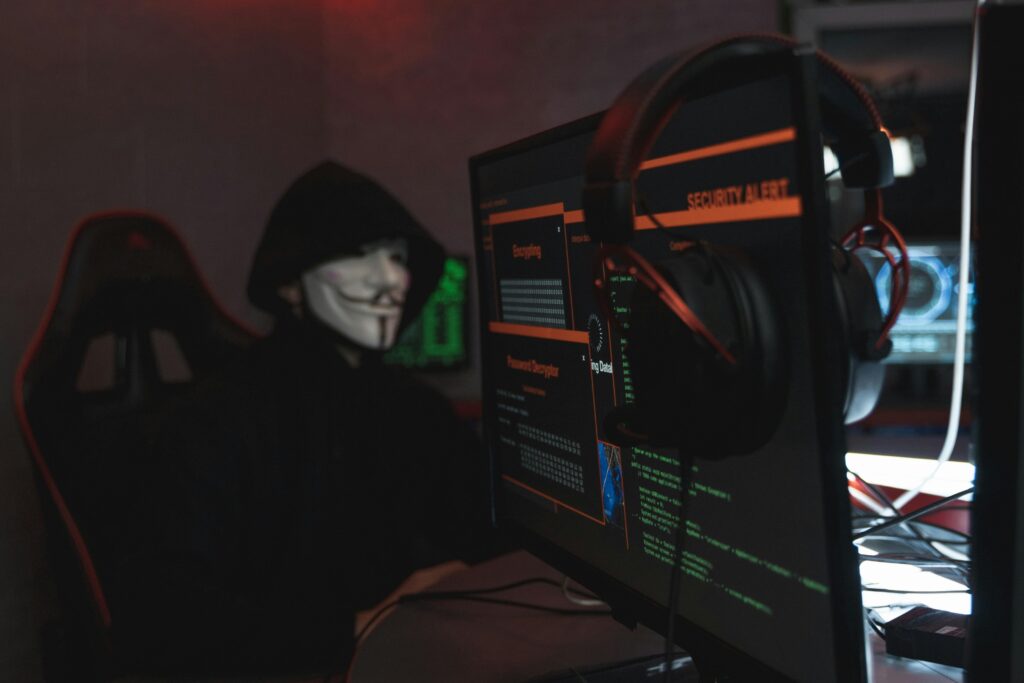 Hacker in a mask using multiple computer screens with a security alert displayed, representing cybersecurity threats for small and medium businesses