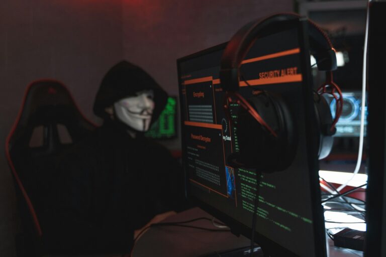 Hacker in a mask using multiple computer screens with a security alert displayed, representing cybersecurity threats for small and medium businesses