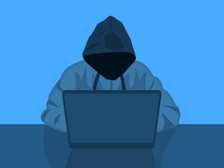 A faceless person in a dark hoodie using a laptop, representing an anonymous hacker or cybercriminal.