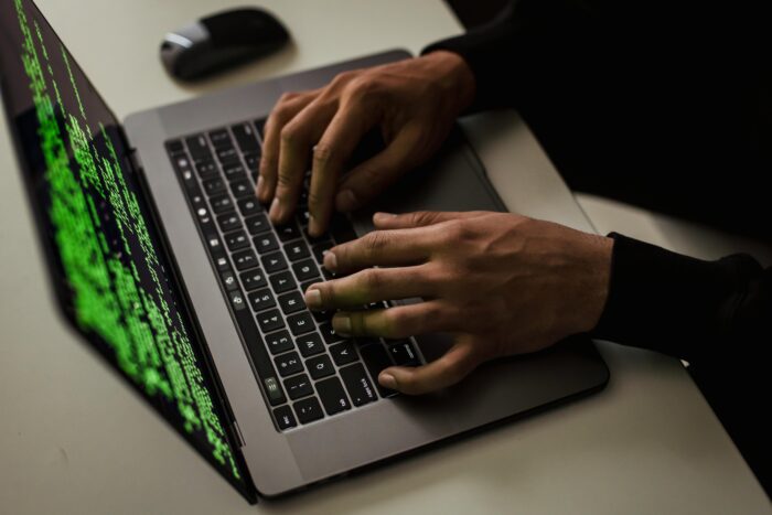 Person typing on a laptop with green code on the screen. Caption